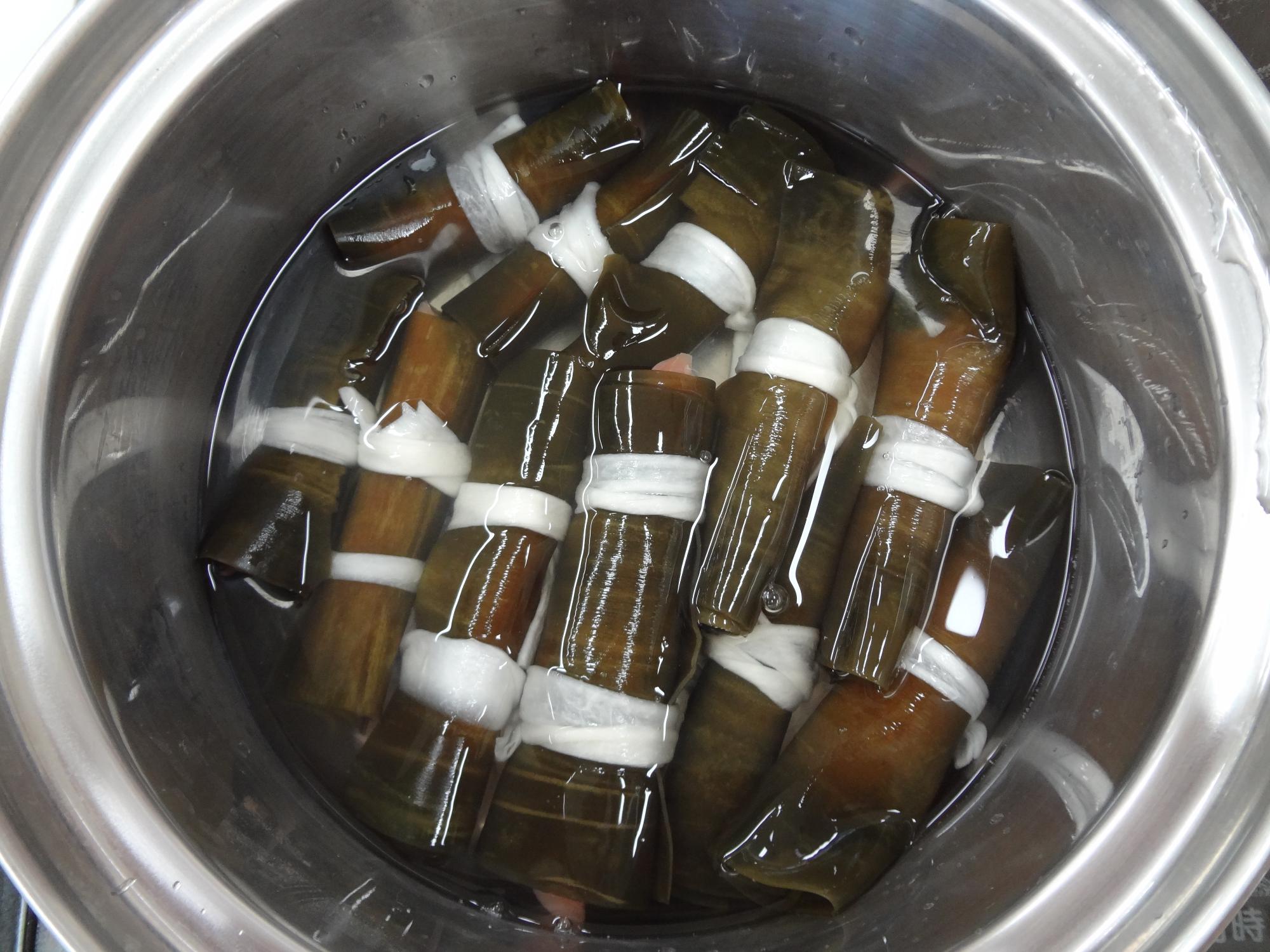 かんぴょうで結んだ沢山の昆布を鍋で煮ている写真