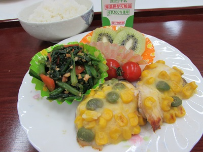お皿の上に鰆のコーンクリーム焼き、緑色のおかずカップに入ったほうれん草のピーナッツ和え、グリーンキウイと、皿の奥に牛乳のラベルとご飯が見える写真