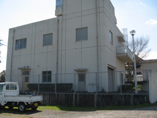 奥に白い建物があり、手前に白い軽トラックが止まっている写真