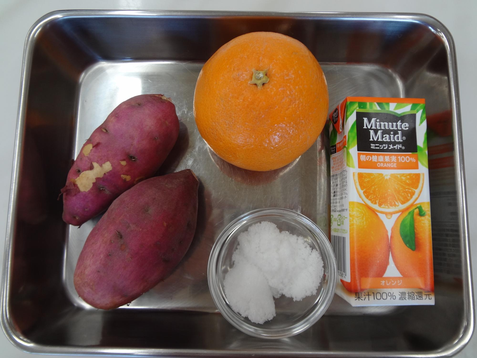 右から紙パックに入ったオレンジジュース、下：砂糖、上：オレンジ、左さつまいも2本がバットに並べられた写真