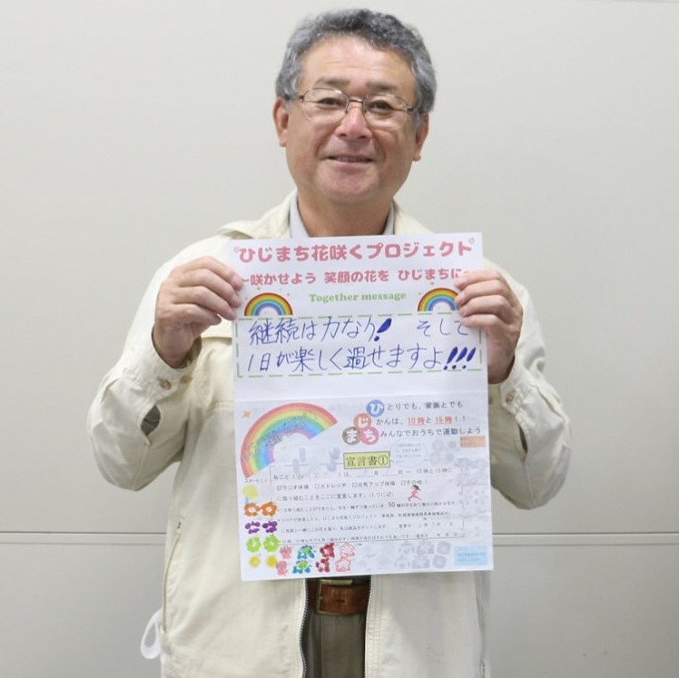 白いシャツを着た男性が、笑顔で両手で宣言書と応援メッセージの用紙を持っている写真