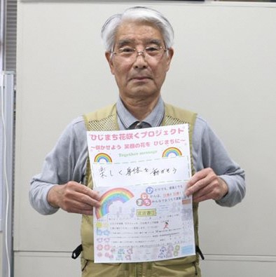 グレー色のシャツを着た男性が、両手で宣言書と応援メッセージの用紙を持っている写真