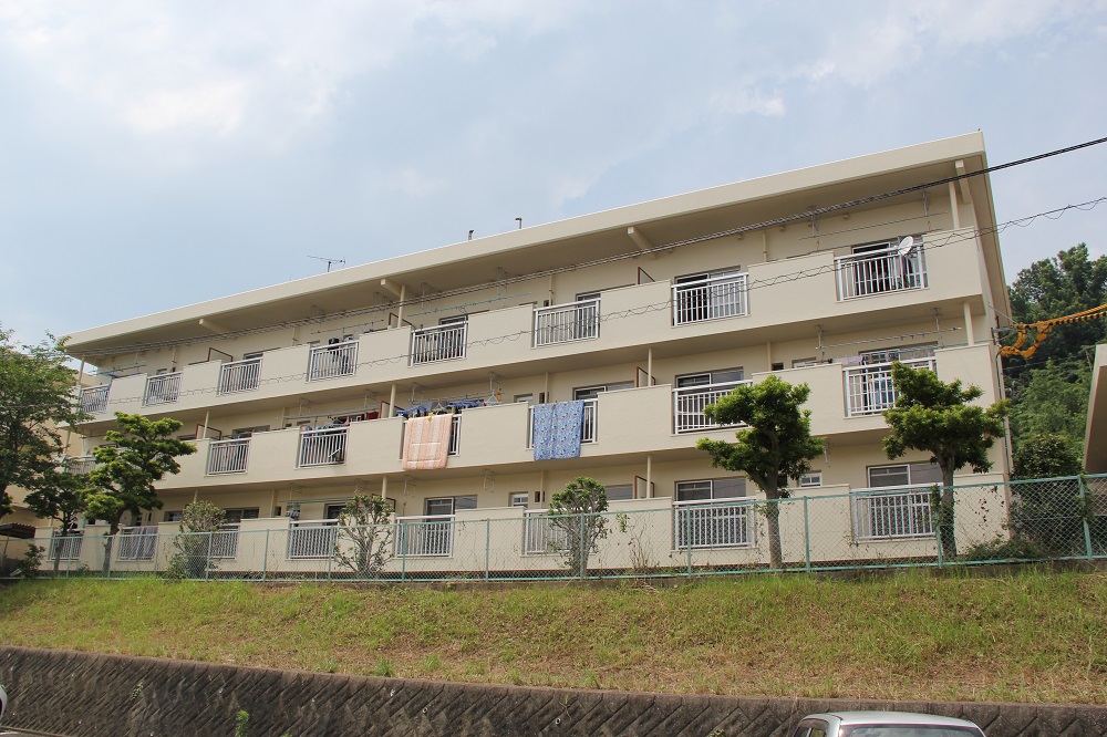 ベランダ側から見えるオフホワイトの外壁の3階建集合住宅（豊岡住宅の外観）の写真