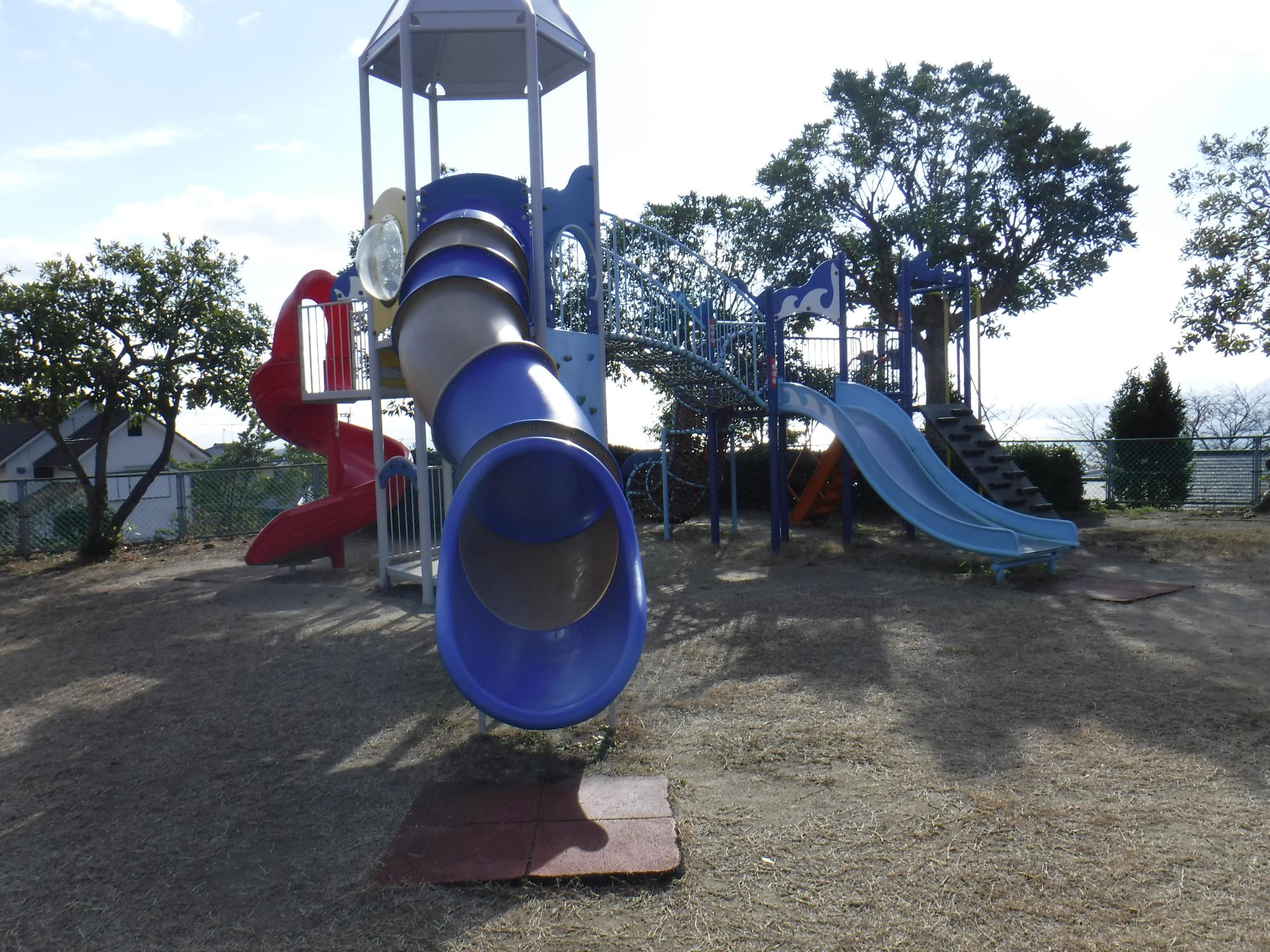 赤い螺旋状の滑り台や青とグレー交互に塗られたトンネル状の滑り台や通常の滑り台がついた複合遊具の写真