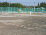 奥に背丈の高い緑のフェンスがある土のテニスコートの写真