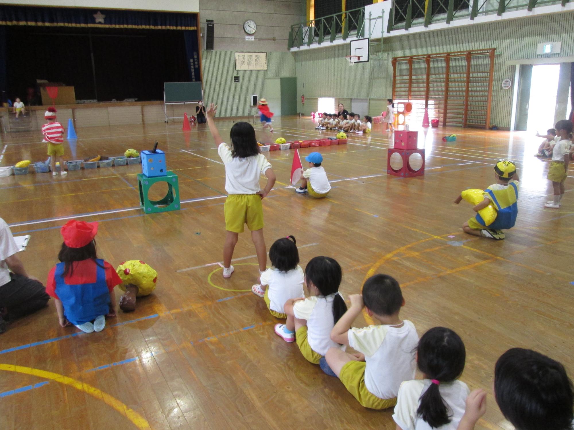 小学校の体育館で、2組に分かれて運動会の競技をする園児の様子の写真