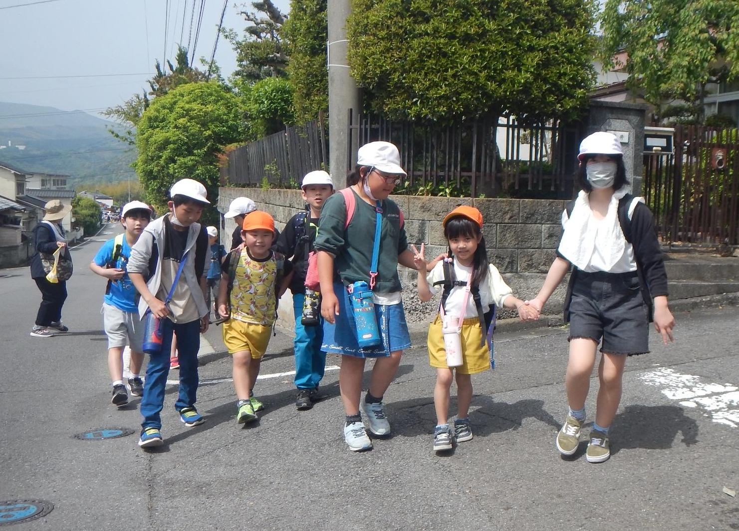 小学生2人と幼稚園児1人で、3人ずつ手をつなぎ仲良く遠足に向かう様子