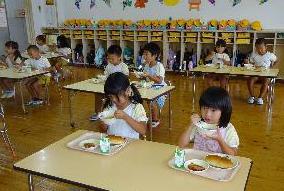 幼稚園児が2人がけの机で給食を食べる写真