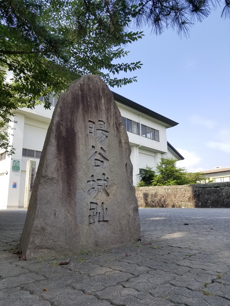 暘谷城址と記された石碑のアップと背景に白い壁の建物が映っている画像