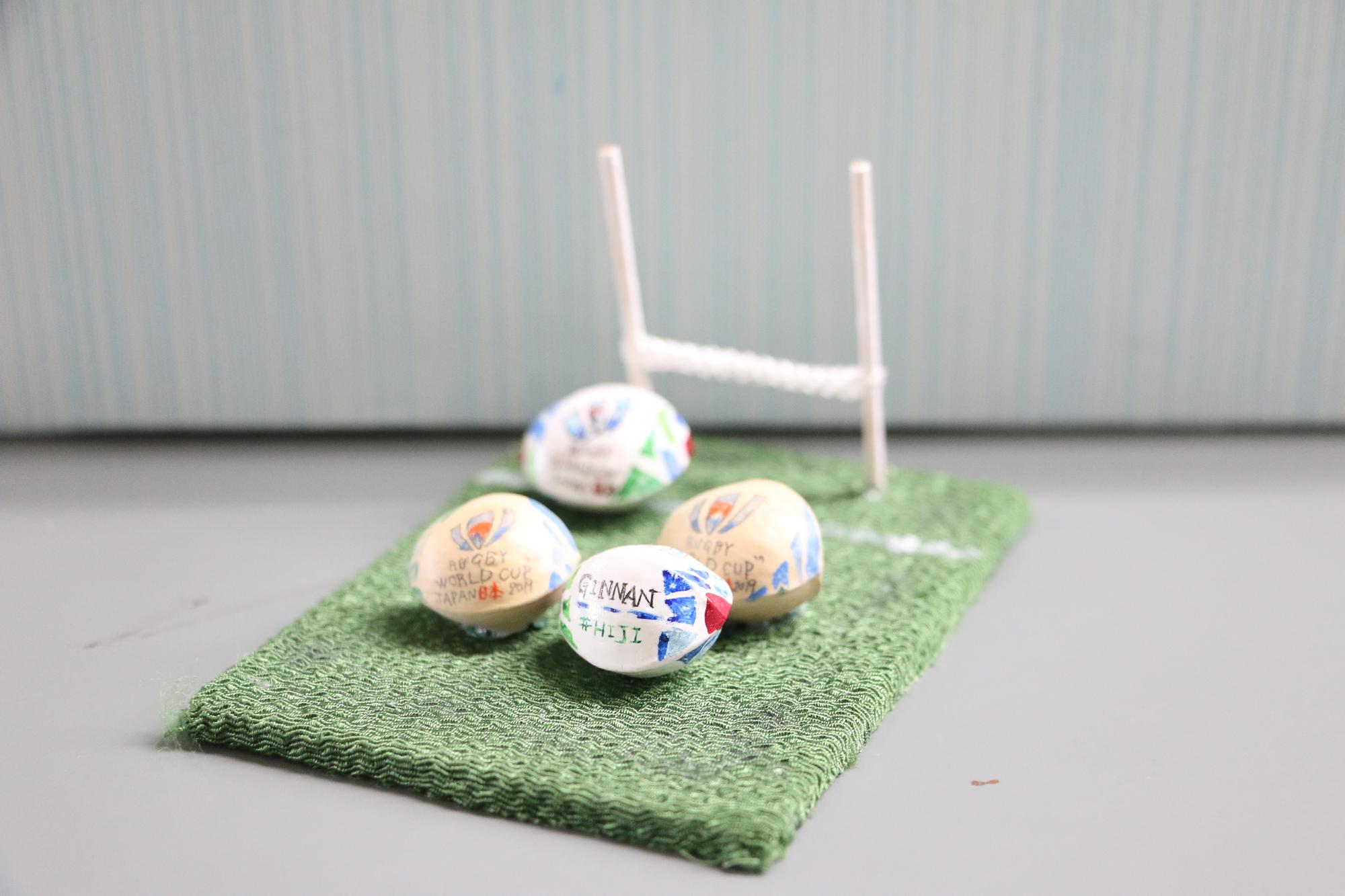 4つのラグビーボールとゴールが芝生を模した布に乗ったミニチュアの模型