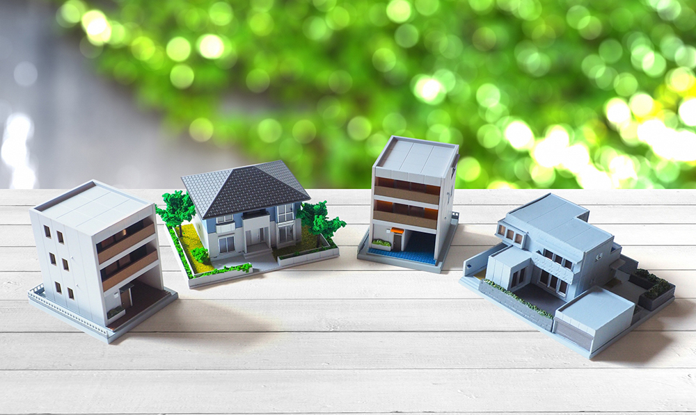 白い木のテーブル上に扇状に並ぶ4つの住宅模型の写真