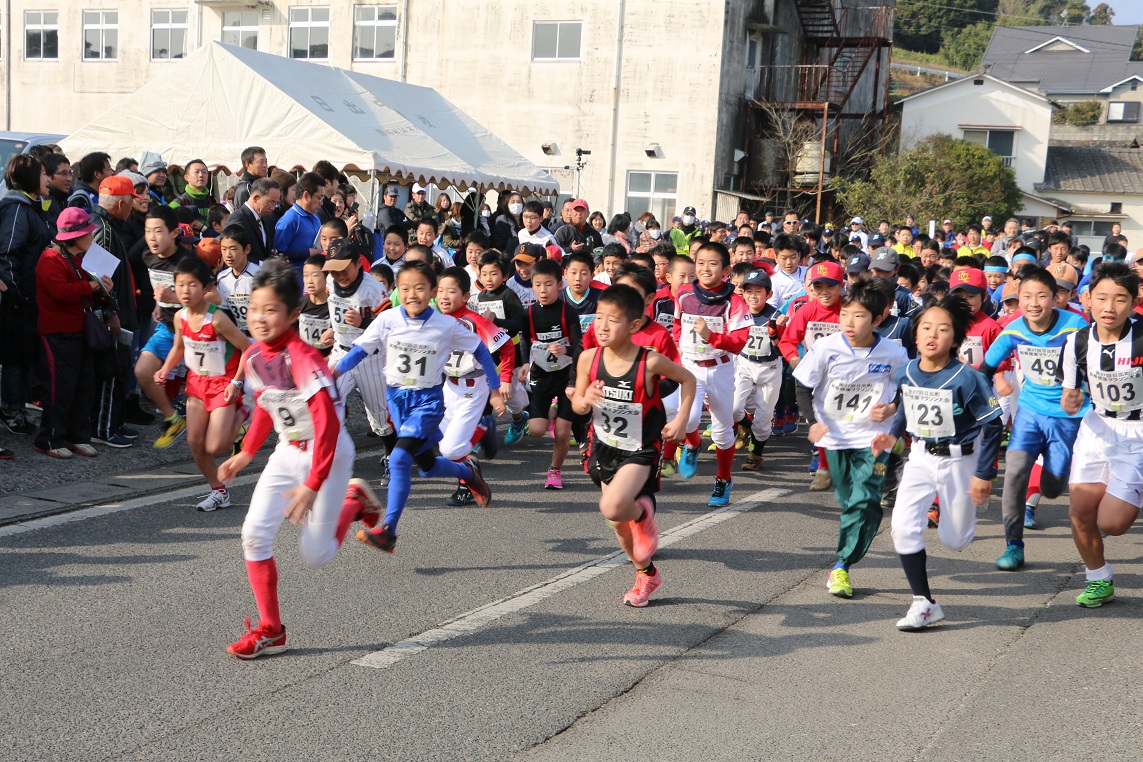 マラソン姿の大勢の子供たちが一斉に走っている様子とそれを道端で応援する大勢の人たちの様子