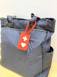 紺色のバッグの取っ手に付けられた、赤色に白色の十字とハートマークのデザインの「ヘルプマーク」の写真